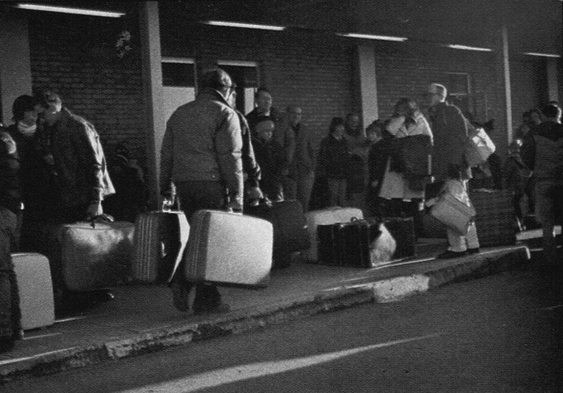 Families with suitcases lined up outside a commissary building at dawn