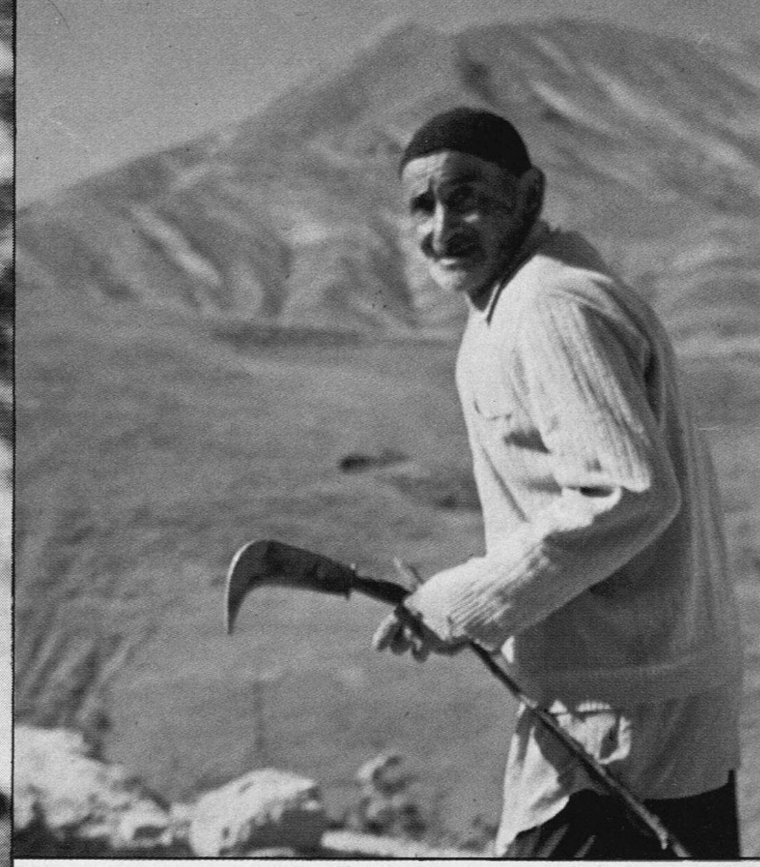 An Iranian farmer carrying a scythe, mountains in the background